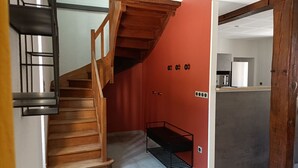 Eine Treppe führt zu einer zweiten Etage, eine rote Wand mit einem schwarzen Metallregal und ein Küchenbereich mit einem weißen Kühlschrank.