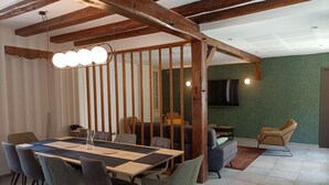 Ein Essbereich mit großem Tisch und Stühlen, Holzbalken an der Decke und einer Wand mit Grüner Struktur.
