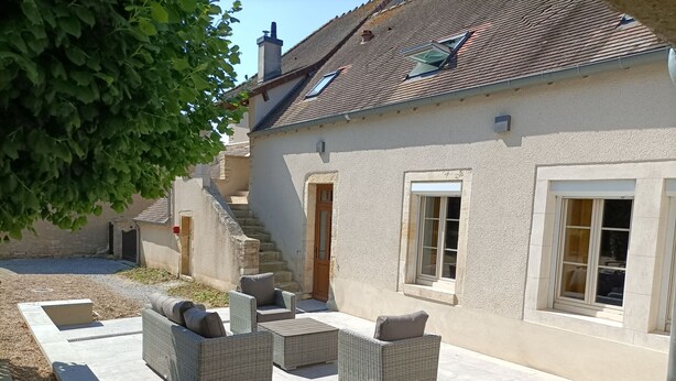 Ein Haus mit einer Terrasse, die Korbmöbel und eine Steintreppe besitzt.