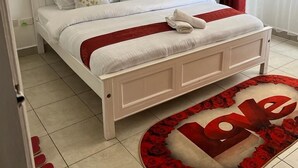 Een slaapkamer met een wit bed, rood-witte beddengoed, een rood-wit tapijt en een raam met rode gordijnen.