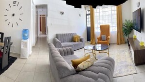 Een moderne woonkamer met een bank, fauteuils, een salontafel en een televisie.