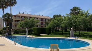 Una piscina con una silla, rodeada de vegetación y un edificio con balcones.