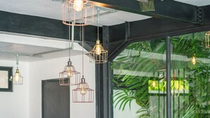 A modern living room with a grey sectional sofa, hanging pendant lights, and a large window with a view of greenery. - Villa Bali Townhouse (Kerobokan)