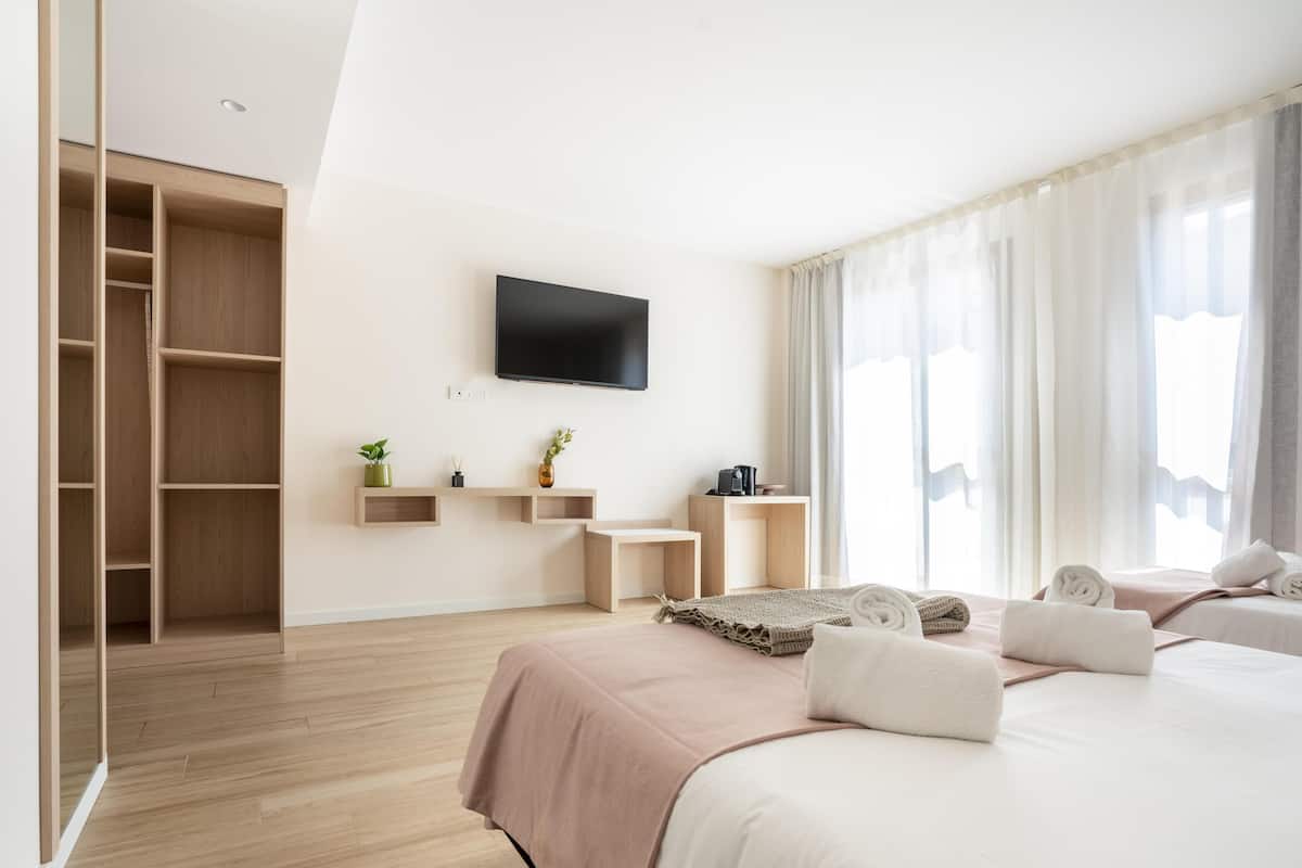 A modern hotel room with a bed, a TV mounted on the wall, a wooden wardrobe, and a bedside table with a lamp and a plant.