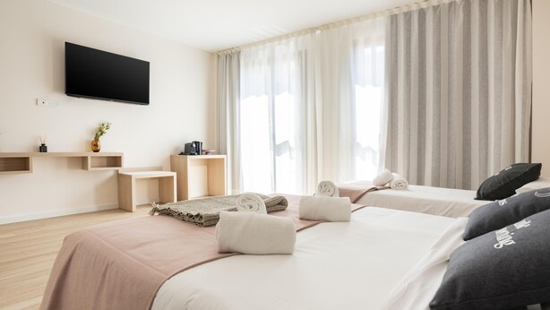 A modern hotel room with a large bed, a flat-screen TV mounted on the wall, a desk with a chair, and a window with curtains. - Limehome Barcelona Carrer de Besalú 82 (Barcelona)