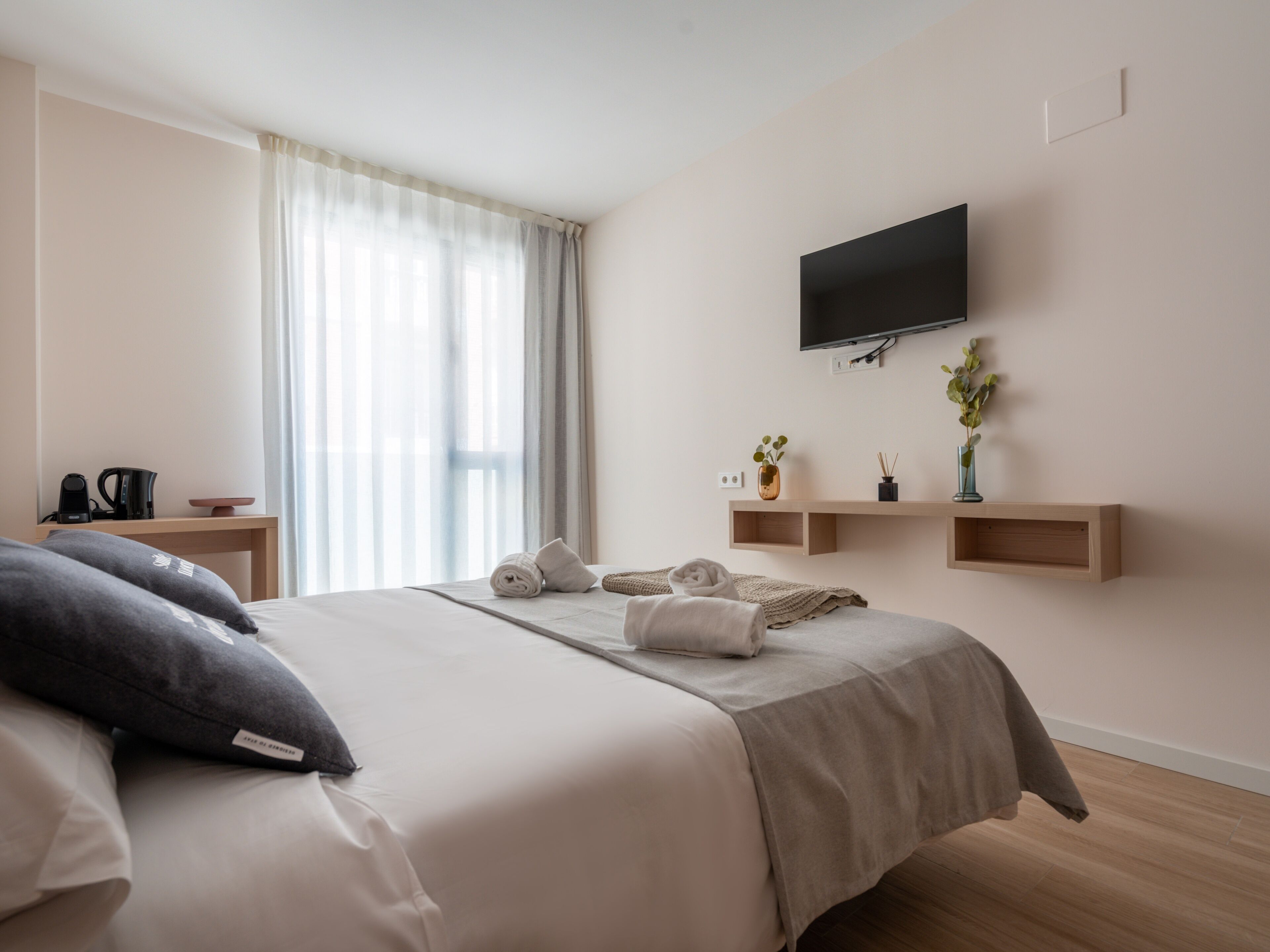 Habitación de hotel con cama, televisor en la pared y ventana con cortinas.