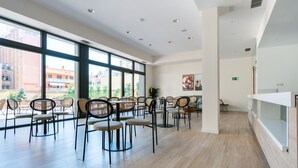 A spacious room with large windows, a dining area with chairs and tables, and a white reception desk. - Limehome Barcelona Carrer de Besalú 82 (Barcelona)