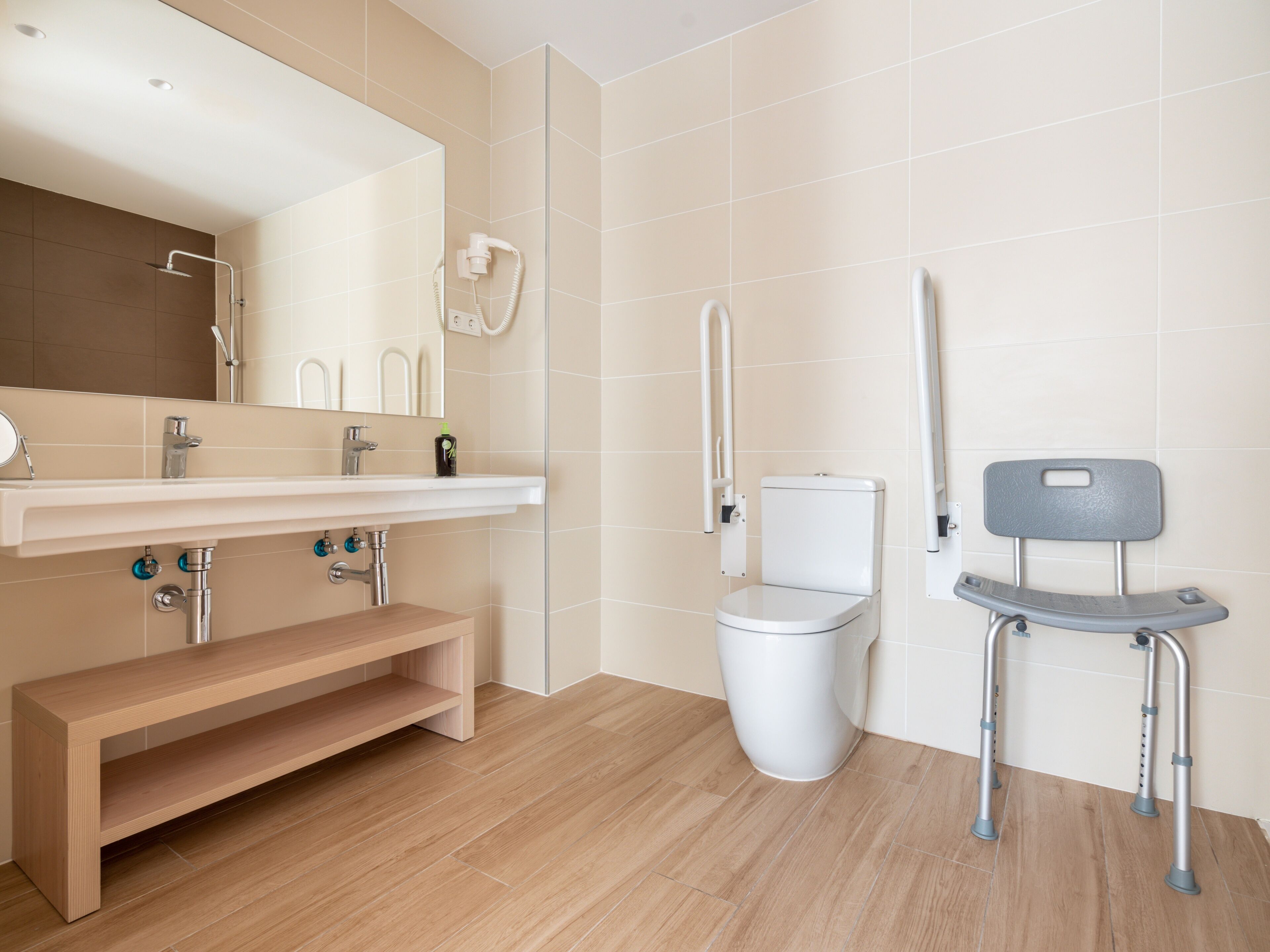 Ein modernes Badezimmer mit Toilette, Waschbecken, einer Bank und einem rollstuhlgerechten Stuhl.