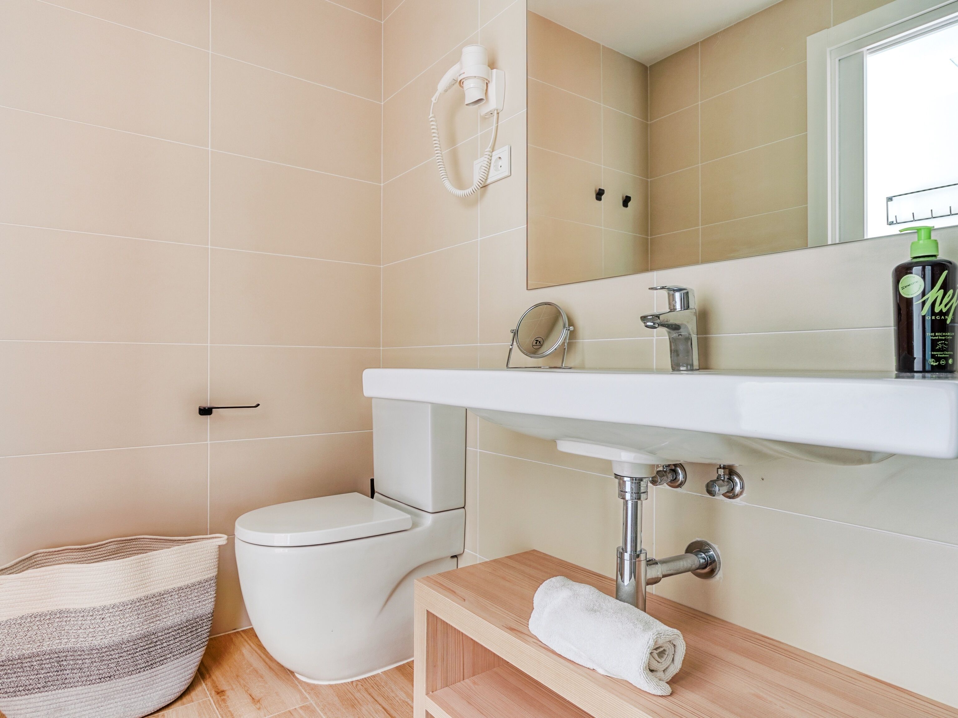 A modern bathroom with a white toilet, a sink with a mirror, and a towel on a wooden shelf.