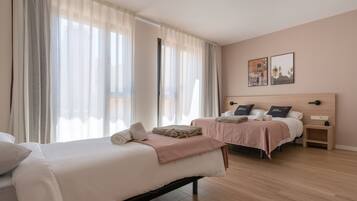 A hotel room with two beds, a wooden floor, and a large window with sheer curtains.