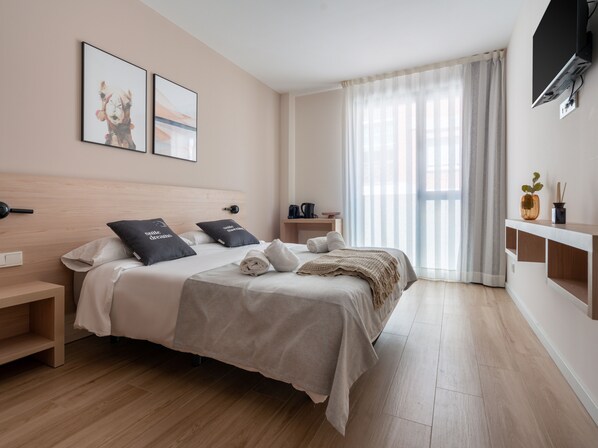 A modern hotel room with a large bed, a bedside table, a TV mounted on the wall, and a window with sheer curtains. - Limehome Barcelona Carrer de Besalú 82 (Barcelona)