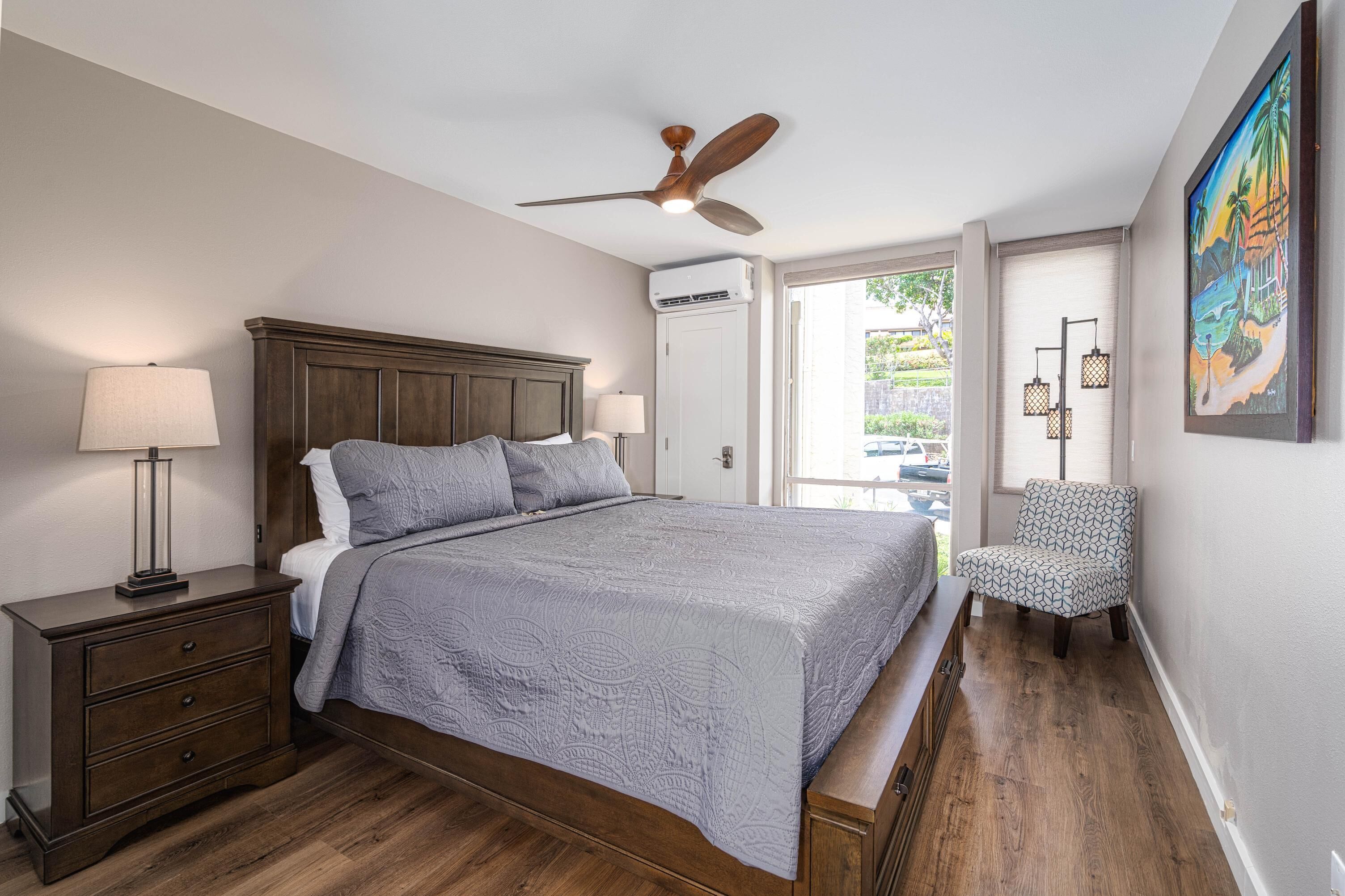 Une chambre à coucher avec un lit, des tables de chevet, un ventilateur de plafond, une chaise et un tableau au mur.
