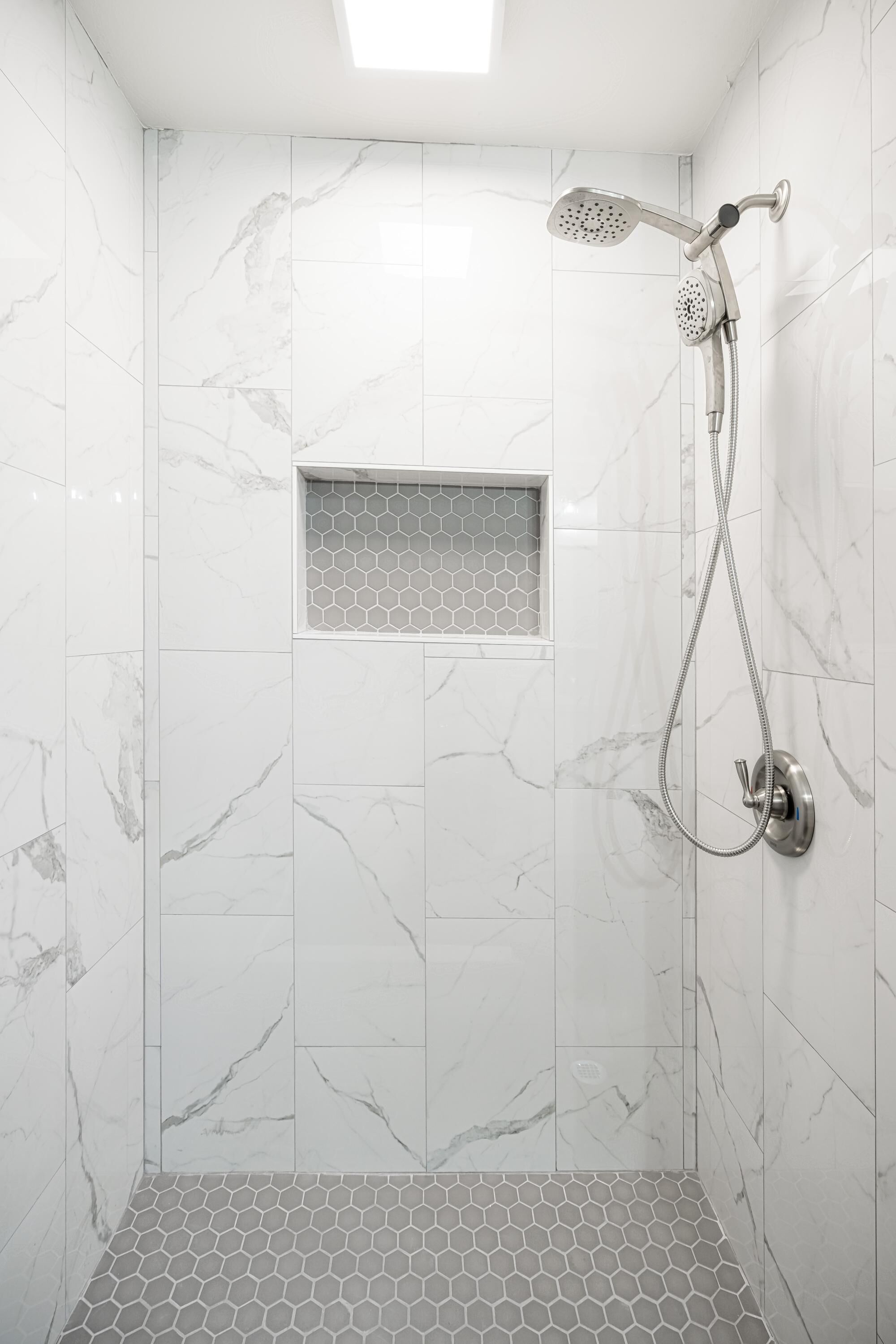 A shower with a handheld showerhead and a wall-mounted faucet, a hexagonal tile pattern on the floor, and a small window with a honeycomb design.