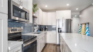 Una cocina moderna con armarios blancos, electrodomésticos de acero inoxidable, encimera de mármol y suelo de madera.