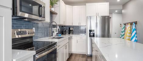 A modern kitchen with white cabinets, stainless steel appliances, a marble countertop, and a wooden floor.