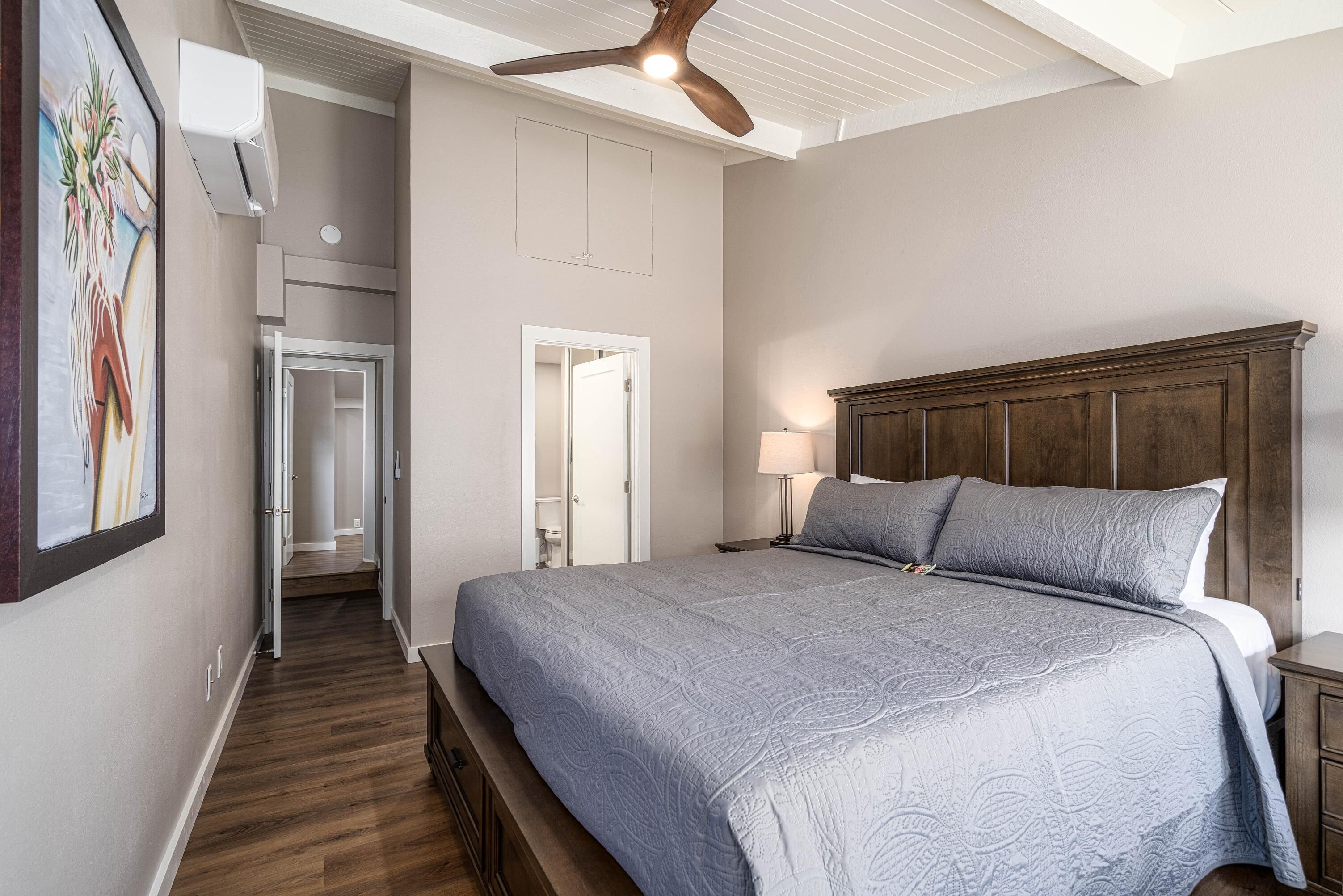 A bedroom with a large bed, wooden headboard, a ceiling fan, and a hallway leading to another room.