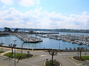 A marina with numerous boats docked, a road with a roundabout, and a coastal landscape in the background. - Charming Apartment with WIFI, Terrace and Parking near Perros-Guirec Marina (Perros-Guirec)
