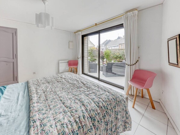 A bedroom with a large bed, a window with curtains, a chair, and a radiator.
