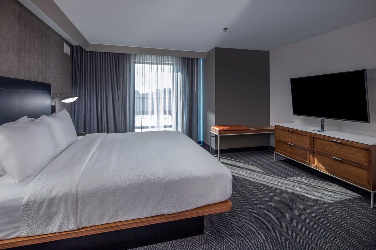 Habitación de hotel con una cama grande, televisor de pantalla plana, escritorio y ventana con cortinas.