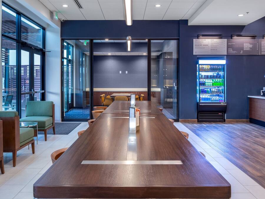 A modern conference room with a long wooden table, comfortable seating, a vending machine, and a view through large windows.