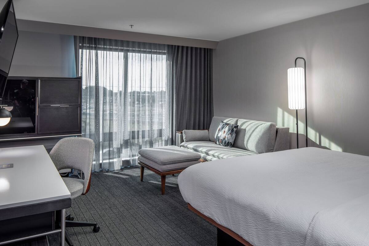 A modern hotel room with a large bed, a sofa, a desk, and a TV.