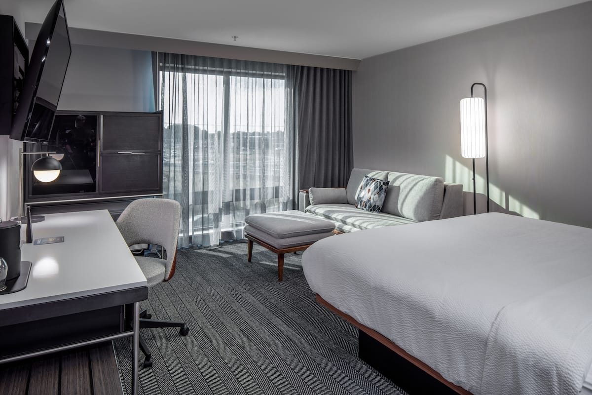 A modern hotel room with a large bed, a desk with a computer, a sofa, and a TV.