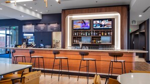 A modern bar area with wooden bar counters, multiple TVs, and a variety of liquor bottles. - Courtyard by Marriott Conway (Conway)