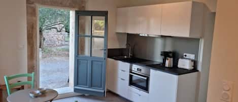 A compact kitchen with white cabinets, a black countertop, and a small dining area with a table and chairs.