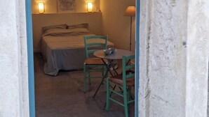 Ein kleiner, rustikaler Raum mit einem Bett, zwei Stühlen, einem Tisch und zwei Wandleuchten.
