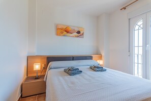 A neatly made bed with a headboard, two bedside lamps, and a painting on the wall.