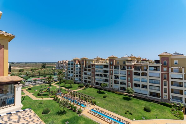 Een hotel met meerdere verdiepingen, een zwembad, groene gazons en een helderblauwe lucht.