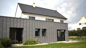 Una casa moderna de dos pisos con techo plano, ventanas amplias y un césped cuidado.