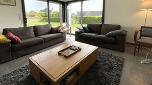 Una sala de estar moderna con dos sofás, una mesa de centro y vistas a un jardín a través de amplios ventanales.
