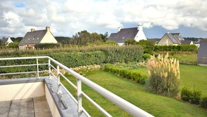 Una terraza con barandilla de metal, suelo de piedra y vistas a casas y vegetación.