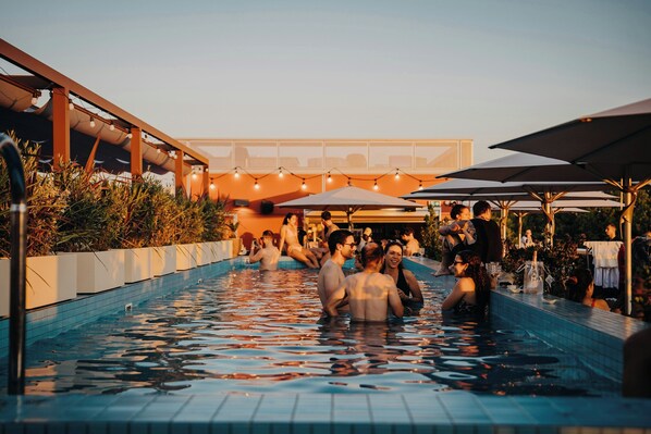 A swimming pool with people, umbrellas, and string lights.