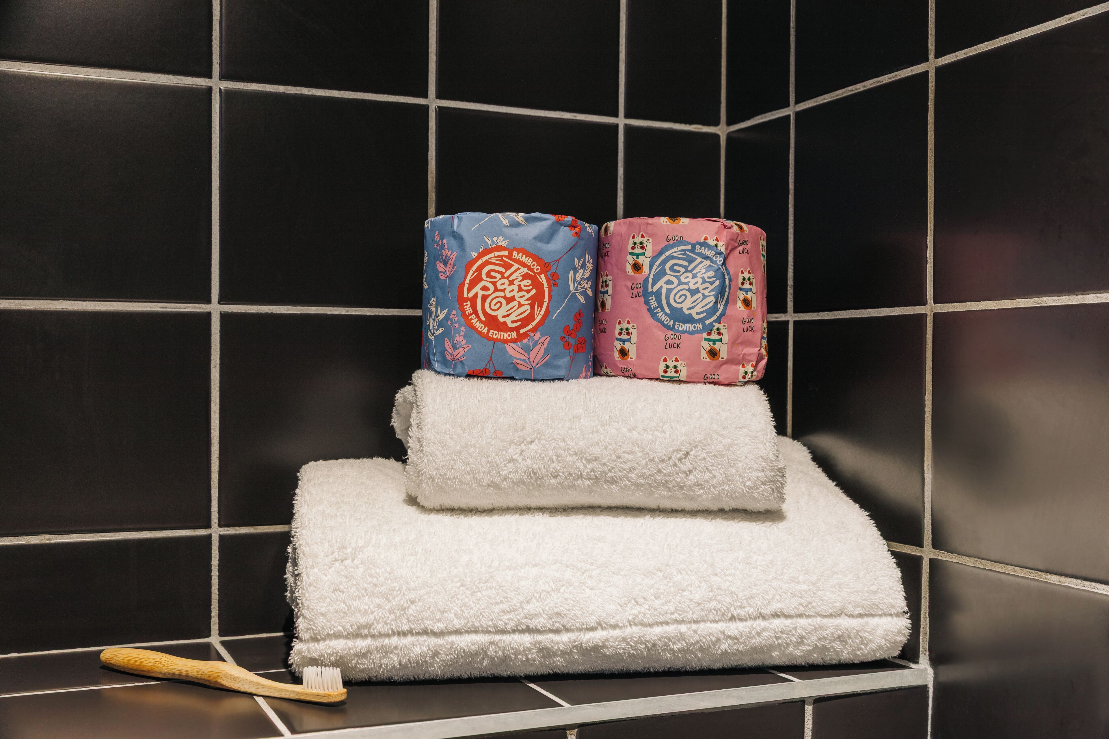 A bathroom with black tiled walls, a white towel, and two rolled towels with floral patterns.