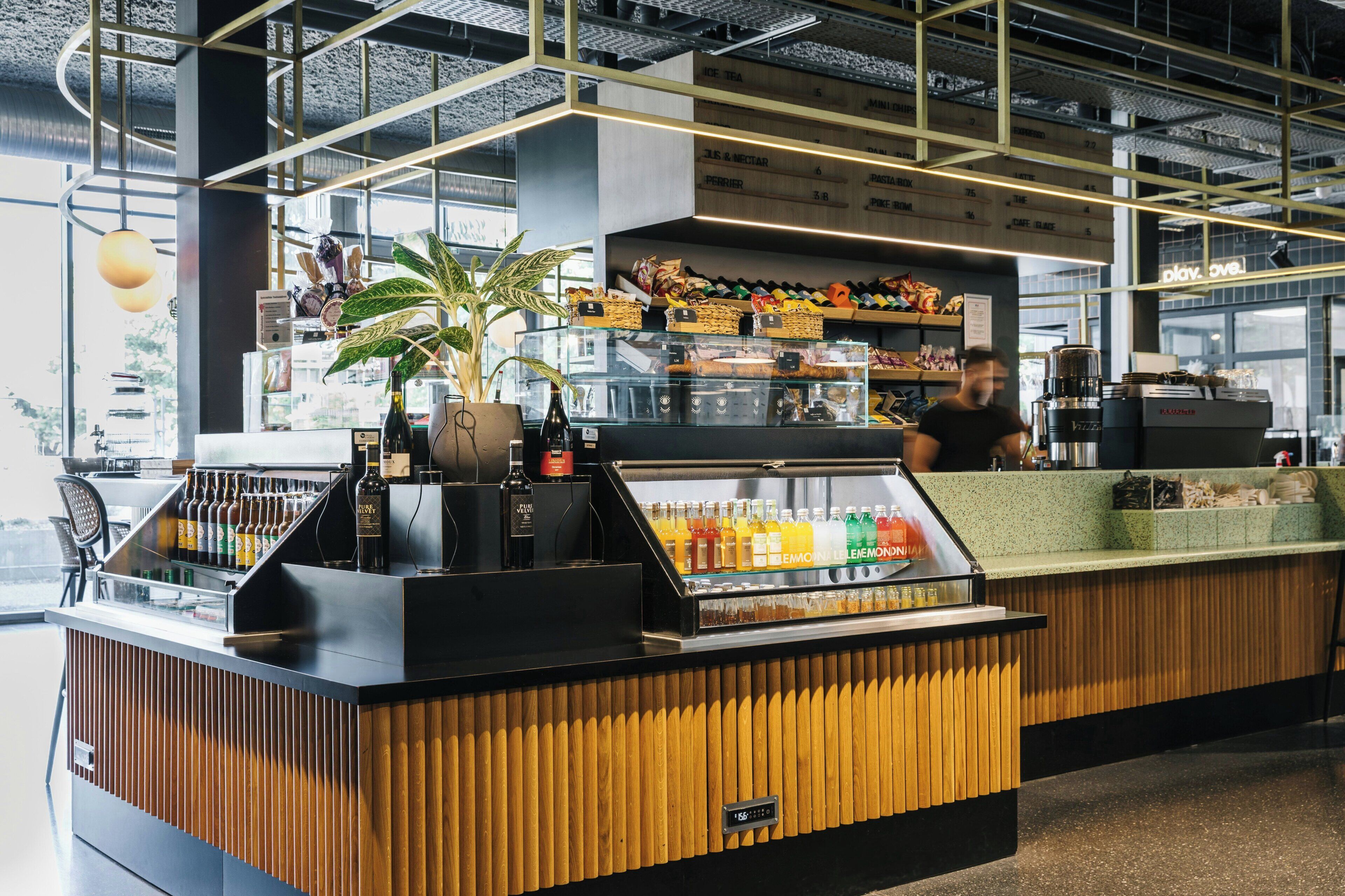 A modern bar area with a wooden counter, a glass display case with beverages, and shelves stocked with snacks.