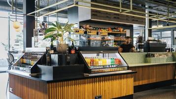 A modern bar area with a wooden counter, a glass display case with beverages, and shelves stocked with snacks.