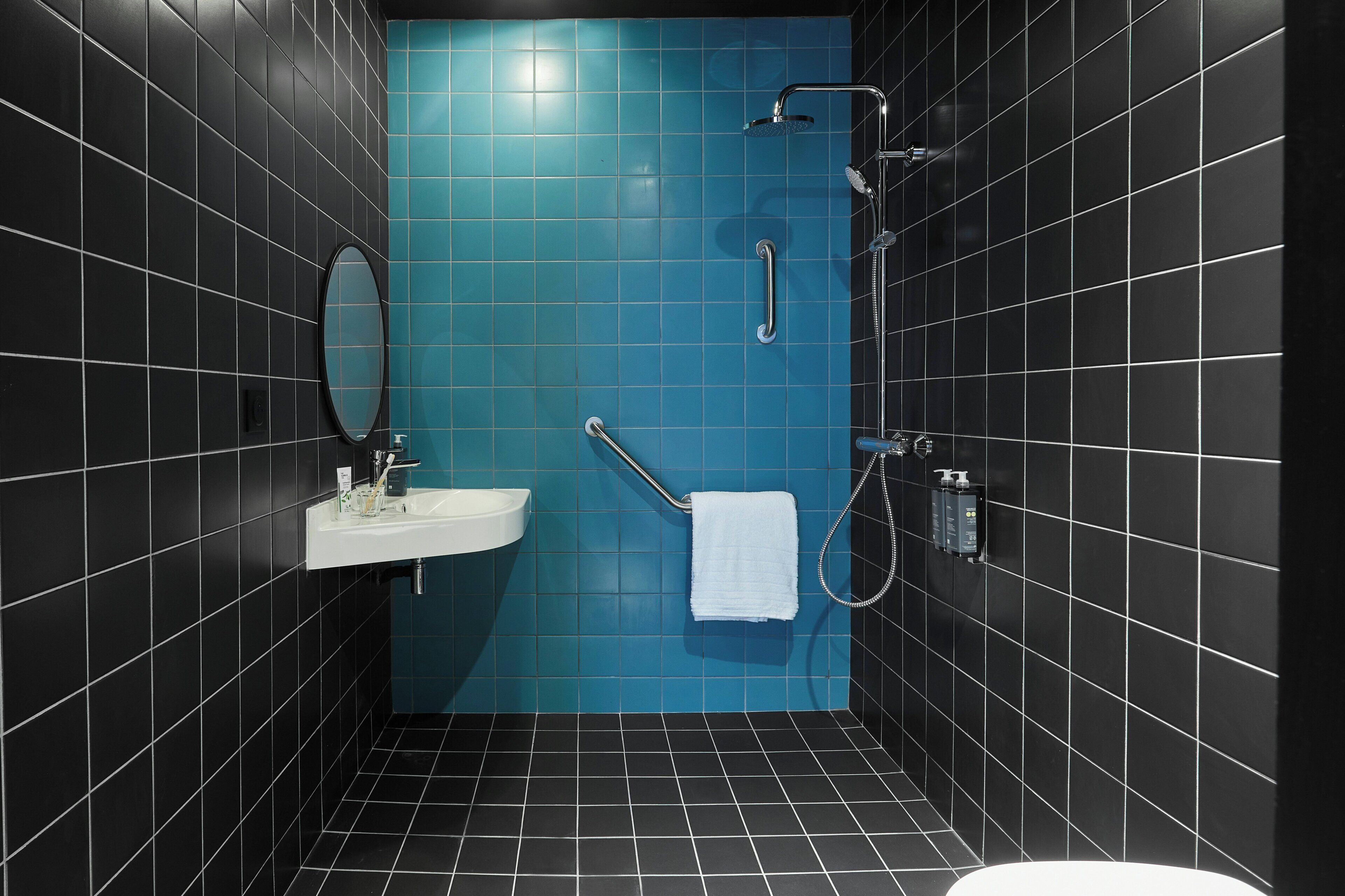 A bathroom with black and blue tiles, a white sink, a mirror, a towel rack, and a shower.