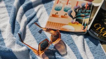 A pair of sunglasses, a magazine, and a book on a striped towel.