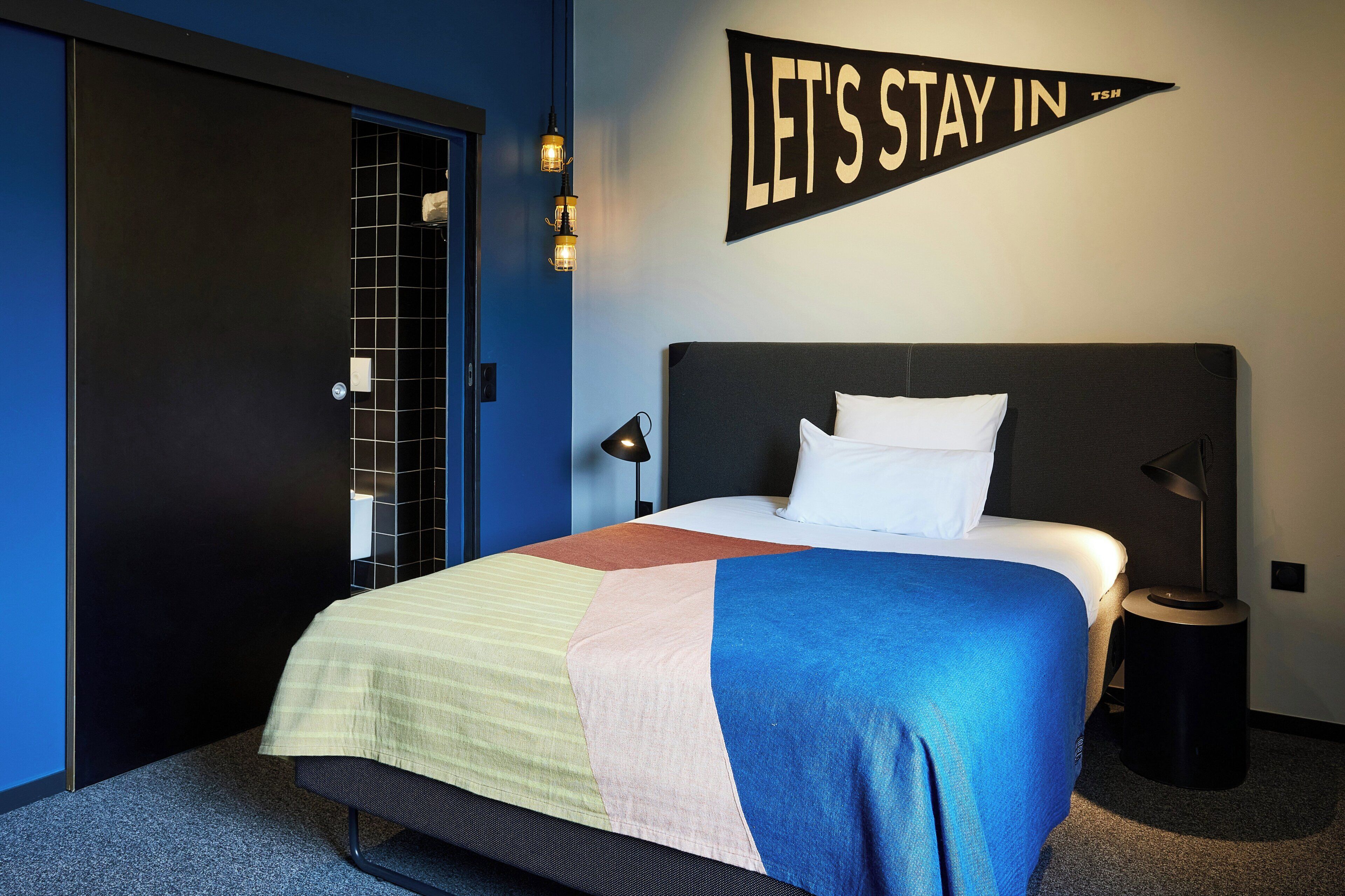 A hotel room with a bed, a wall sign, a door, and a nightstand.