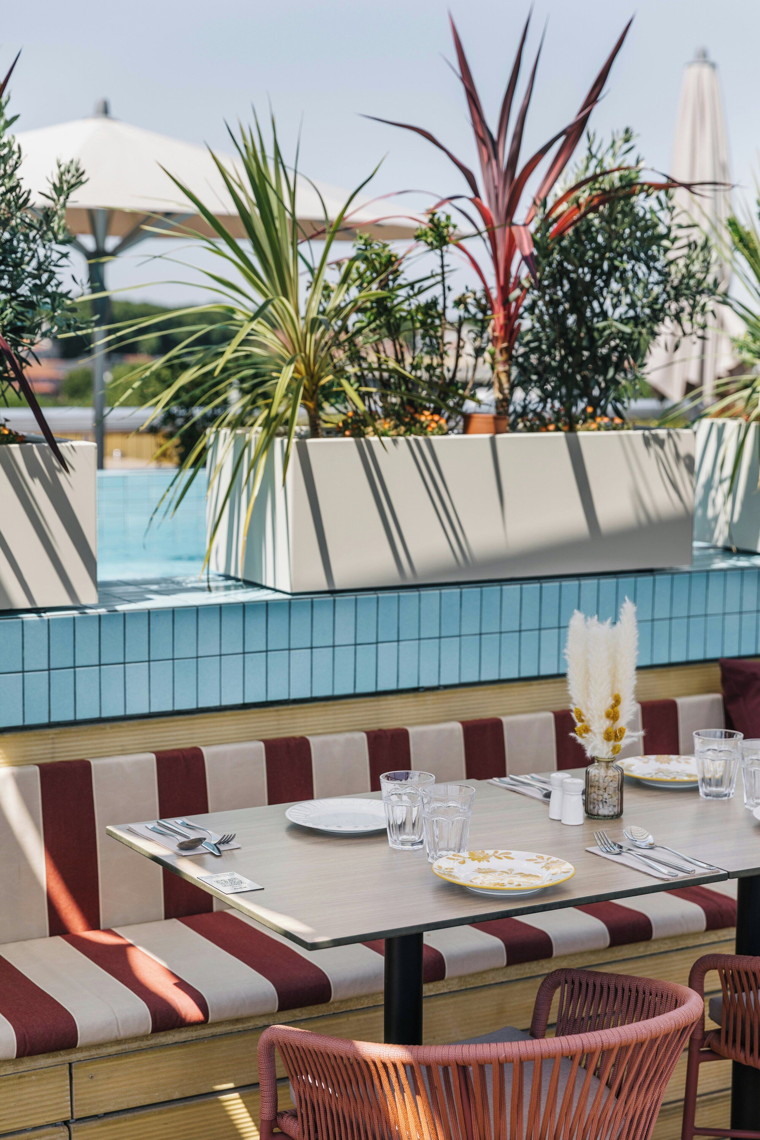 Un espace extérieur aménagé pour les repas, avec une piscine, des sièges à rayures et des plantes en pot.