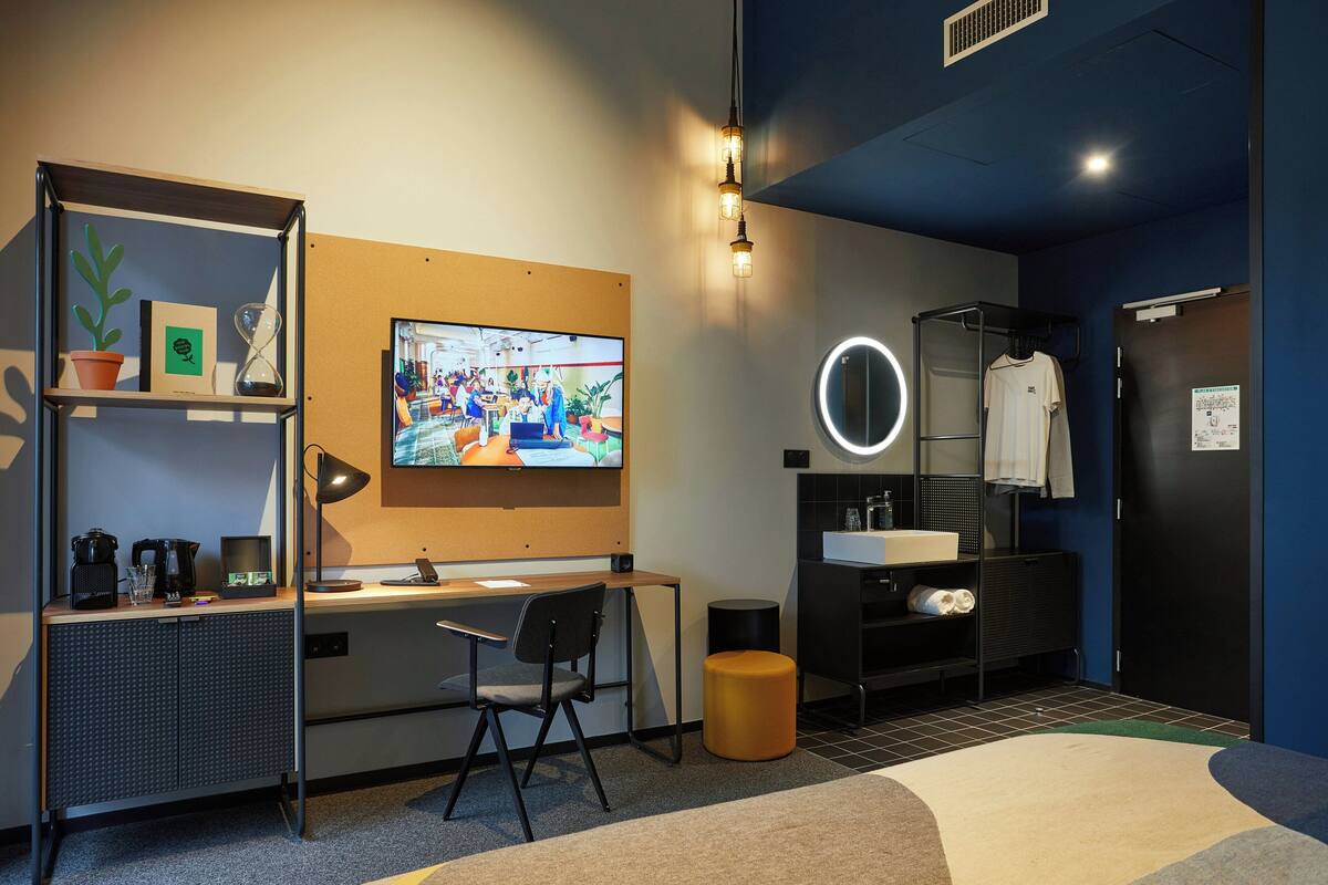 Een moderne hotelkamer met een bureau, stoel, televisie en een badkamer met wastafel en spiegel.