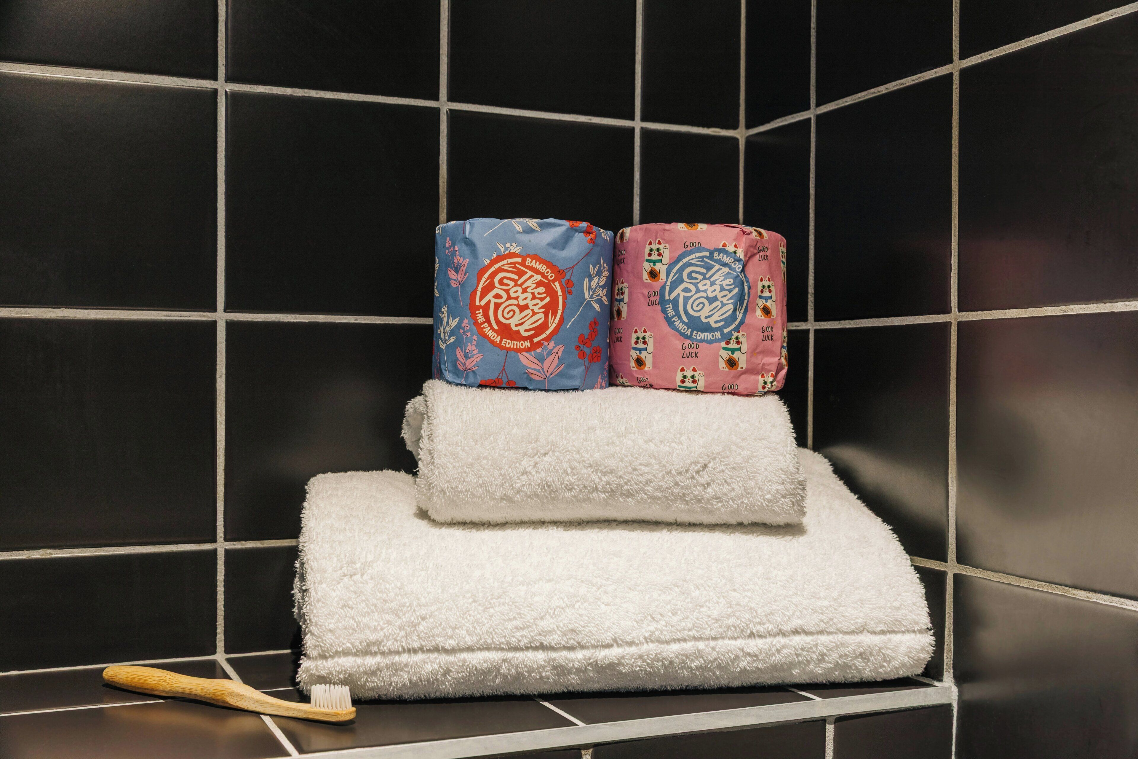 Een badkamer met zwart betegelde muren, een witte handdoek en twee opgerolde handdoeken met bloemenmotieven.