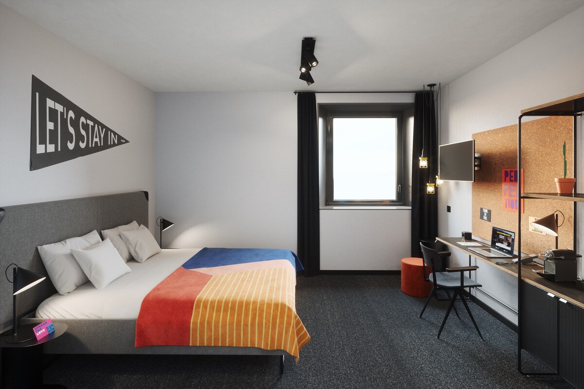 Habitación de hotel con cama, escritorio, computadora y ventana.