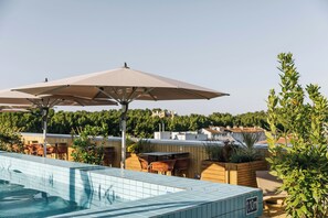 A rooftop pool area with tiled flooring, outdoor seating, and umbrellas.