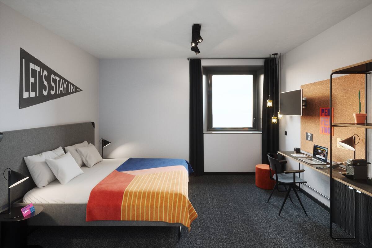 Een hotelkamer met een bed, bureau, computer en een raam.
