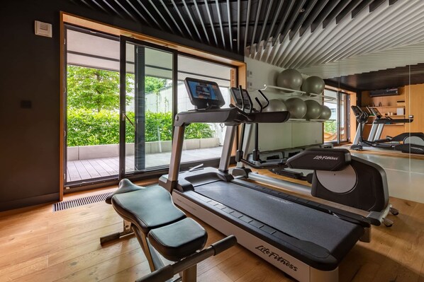 A modern gym with a treadmill, elliptical, and exercise balls.