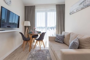 A modern living room with a flat-screen TV, a sofa, a dining table with chairs, and a window with curtains.