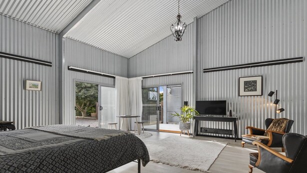 A spacious bedroom with a large bed, a TV, and a seating area with a chair and a sofa. - The Cubby House by Wine Coast Holiday Rentals (WHITES VALLEY)